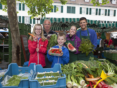 Marktstand mit verschiedenen Obst- und Gemüsesorten und Marktpersonal